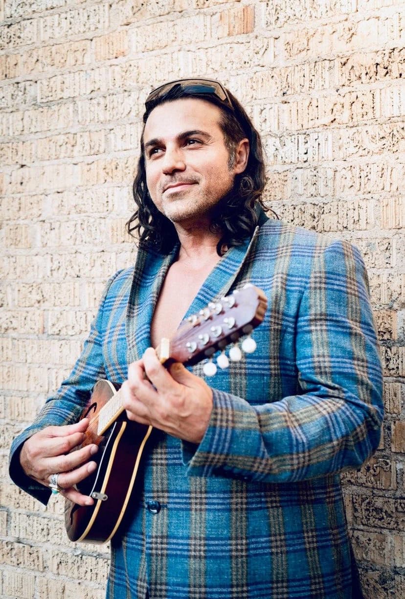 Dr. Ray holding mandolin against brick wall, smiling