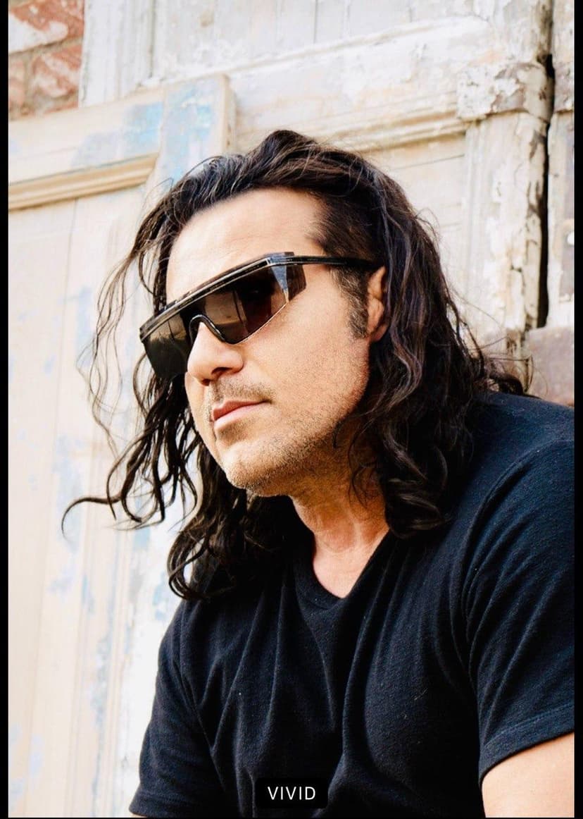 Dr. Ray in black tee and sunglasses, rustic backdrop